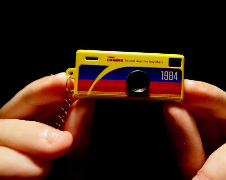 Mão segurando uma mini câmera amarela com o número 1984