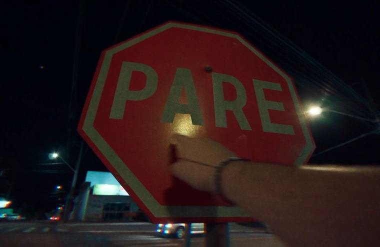 Mão tocando uma placa de PARE numa rua à noite